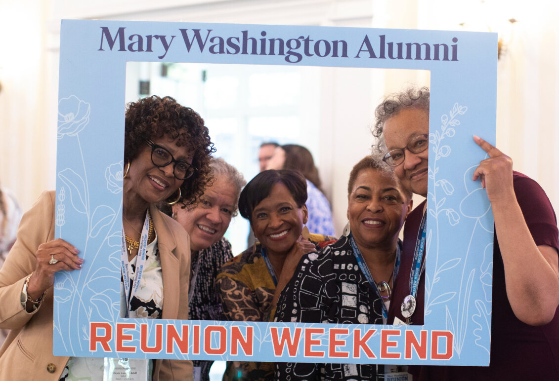 Five 1976 alumnae pose for a photo with a photo frame that reads 'Mary Washington Alumni Reunion Weekend.'
