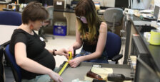 A professor and a student sit in a historic preservation lab and hold a measuring tape against a storage drawer.