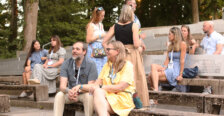 A couple sit on the Heslep Amphitheatre steps during a 'Bites and Sites' event. Other alumni and students stand around in the background.