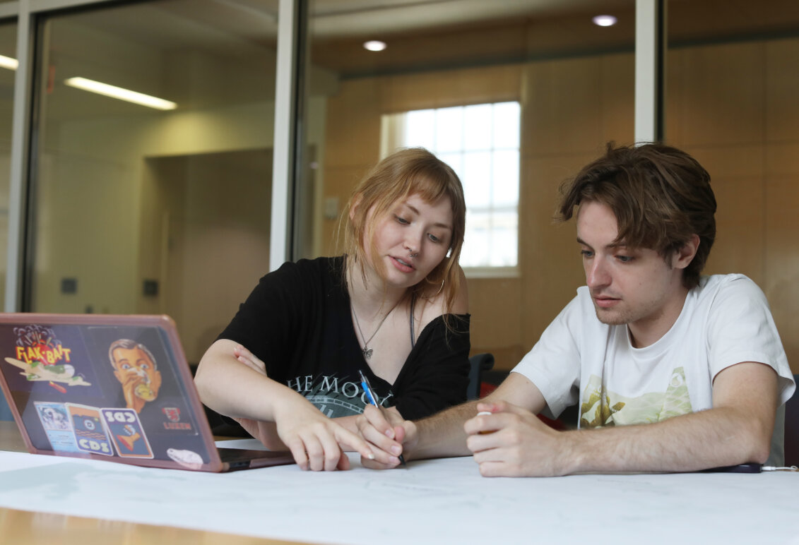 Two students sit at a table with a laptop and work on a map together.