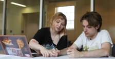 Two students sit at a table with a laptop and work on a map together.