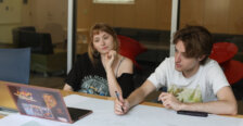 Two students sit in front of a laptop with a map on the table in front of them.