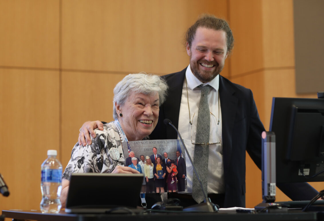 A 1962 alumna thanks her alma mater for a UMW alumni award and is joined by a 2015 alumnus whom she worked with. She holds a photo of herself former Virginia Governor Glenn Youngkin and other public officials at the time the legislation passed.