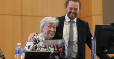 A 1962 alumna thanks her alma mater for a UMW alumni award and is joined by a 2015 alumnus whom she worked with. She holds a photo of herself former Virginia Governor Glenn Youngkin and other public officials at the time the legislation passed.
