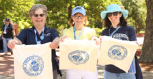Three alumnae standing on Campus Walk hold out the bags they screenprinted with a Mary Washington College logo.