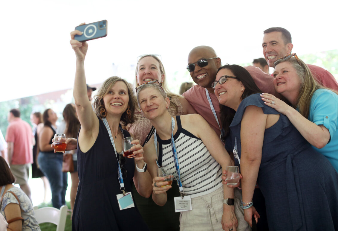A group of 1990s alumni take a selfie while holding wine glasses.