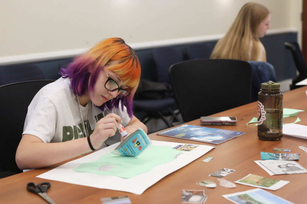 A woman uses a gluestick to attach something to a vision board.