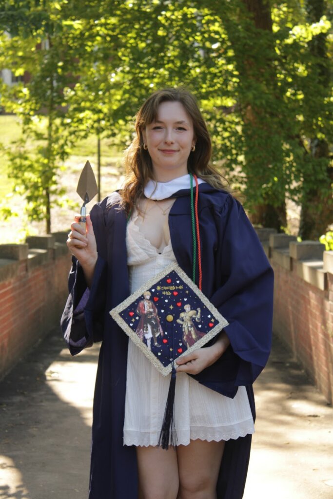 A young woman wearing college graduation regalia and holding a trowel