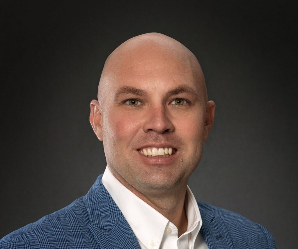 A man in a suit jacket smiles at the camera