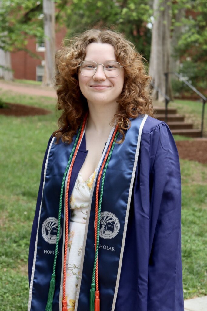 A young woman poses in college graduation regalia