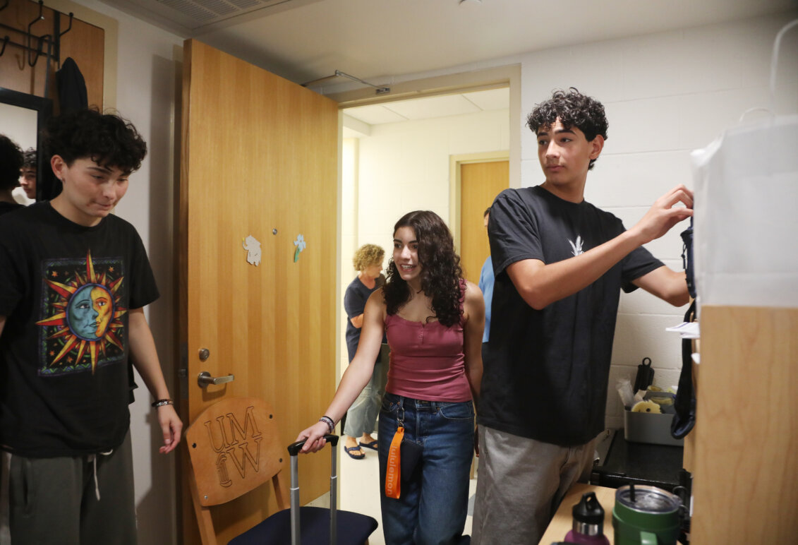 Three people stand inside a college residence hall room