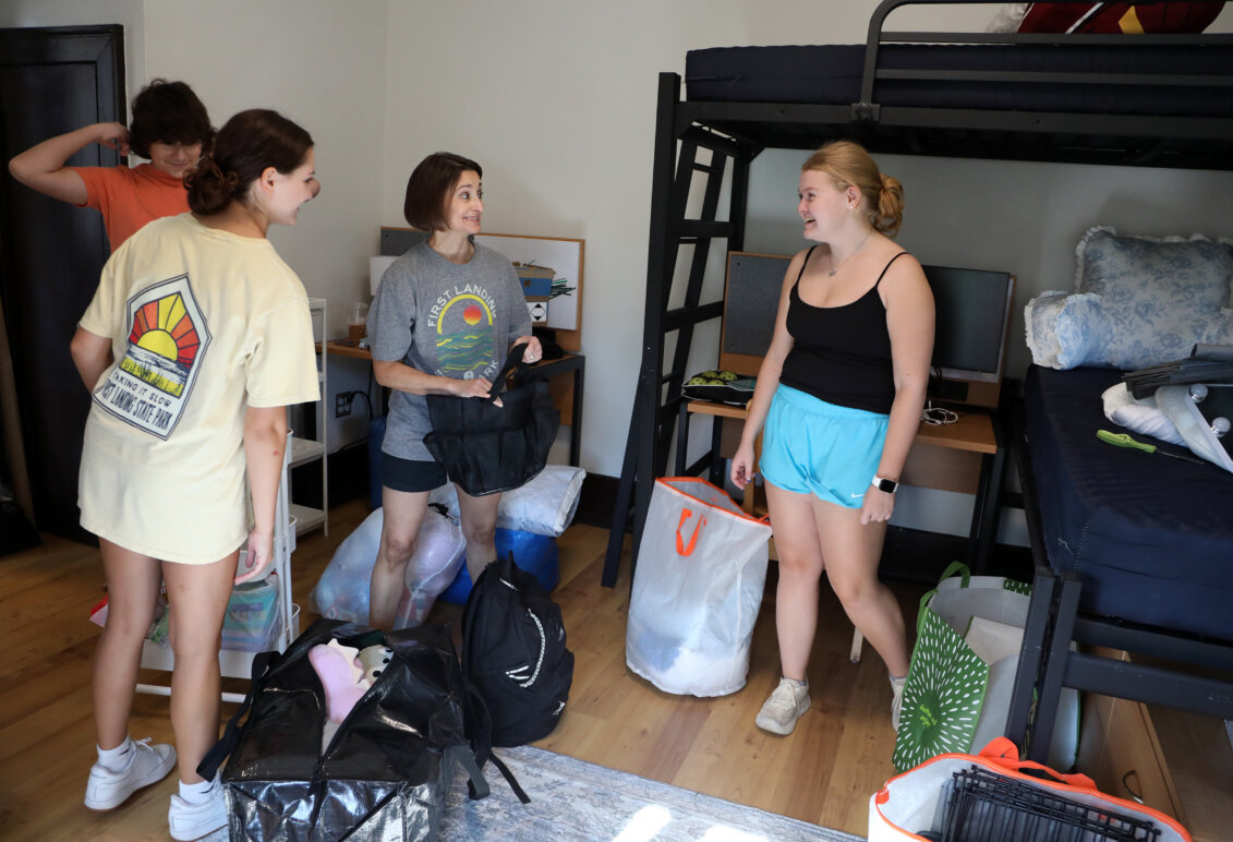 Four people stand in a college residence hall room, surrounded by bags that they're unpacking