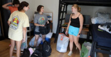Four people stand in a college residence hall room, surrounded by bags that they're unpacking