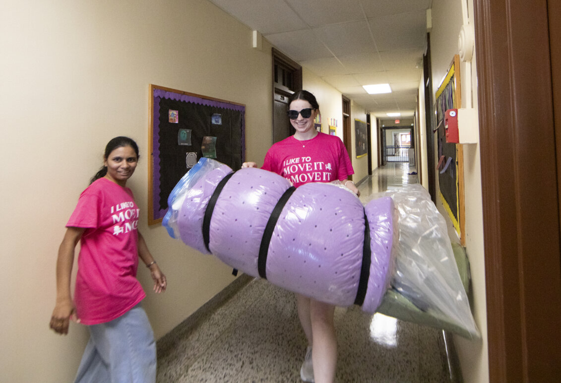 A student walks down a hallway carrying a purple foam mattress pad