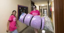 A student walks down a hallway carrying a purple foam mattress pad