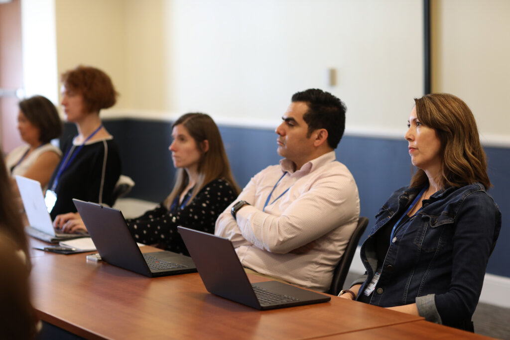 A few people sit in a room listening to a speaker