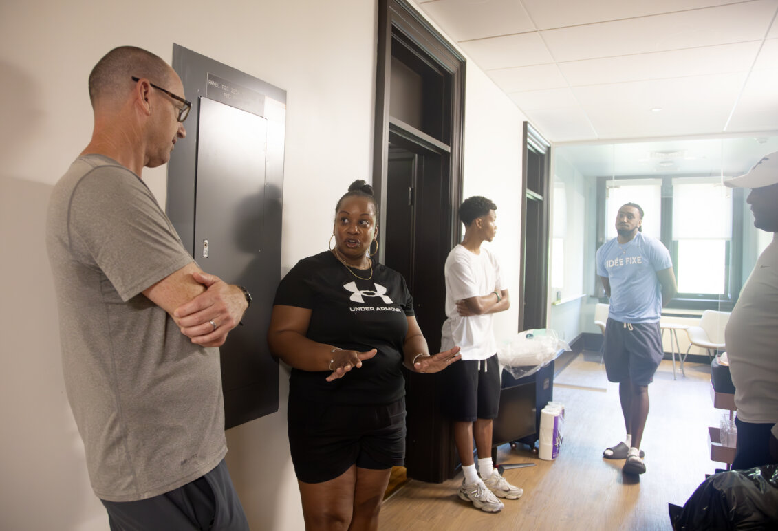Five people - four men and one woman - stand in a hallway talking