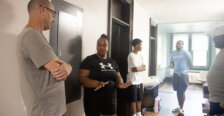 Five people - four men and one woman - stand in a hallway talking