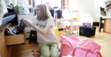A student sits on the floor of a residence hall, pulling something out of a drawer under the bed