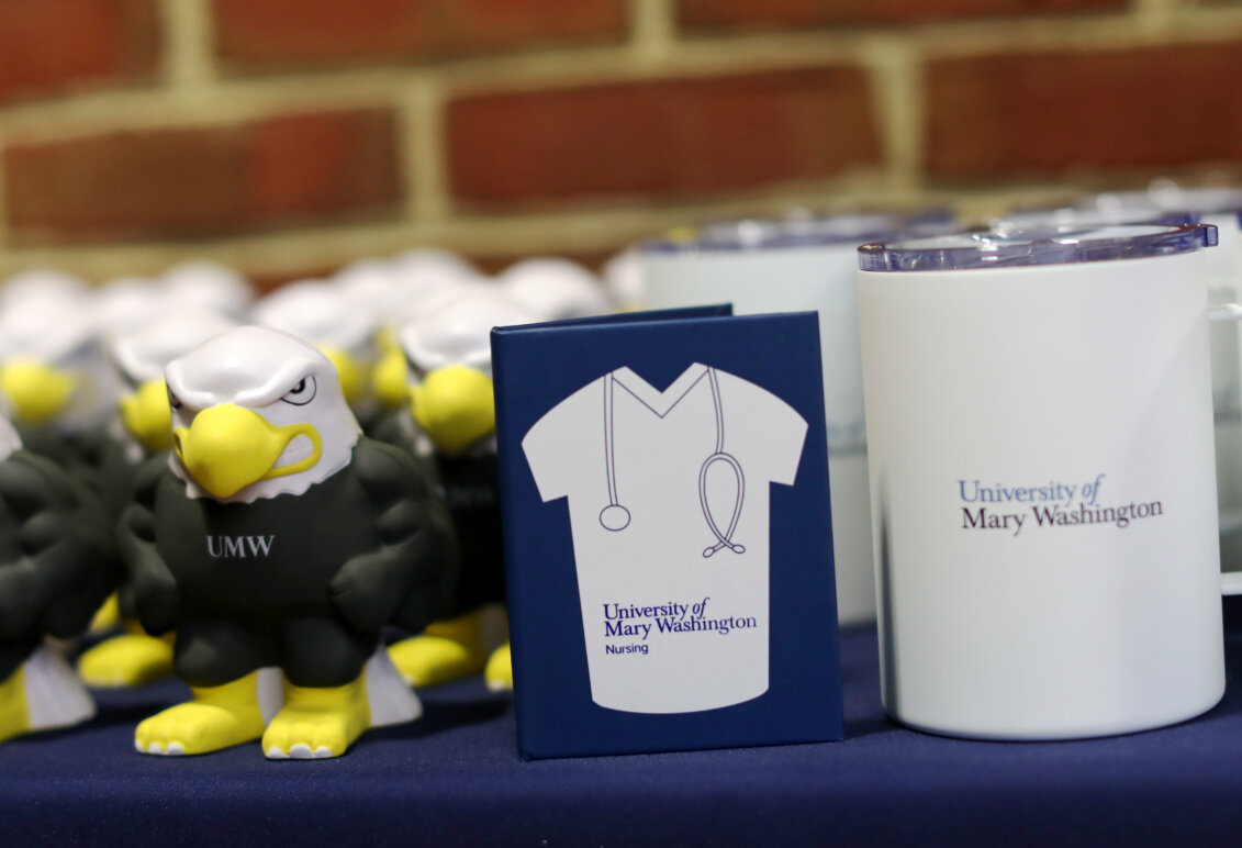 Mementos, like Eagle squish toys, notebooks emblazoned with lab coats and stethoscopes, and portable cups, line a table against a brick wall