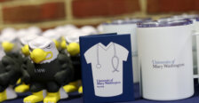 Mementos, like Eagle squish toys, notebooks emblazoned with lab coats and stethoscopes, and portable cups, line a table against a brick wall