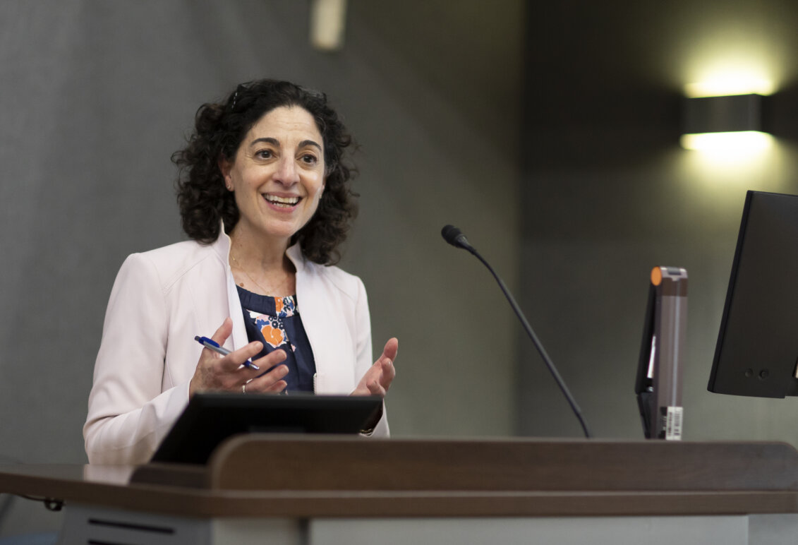 A smiling woman stands at a podium with a pen in her hand.