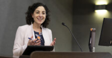 A smiling woman stands at a podium with a pen in her hand.