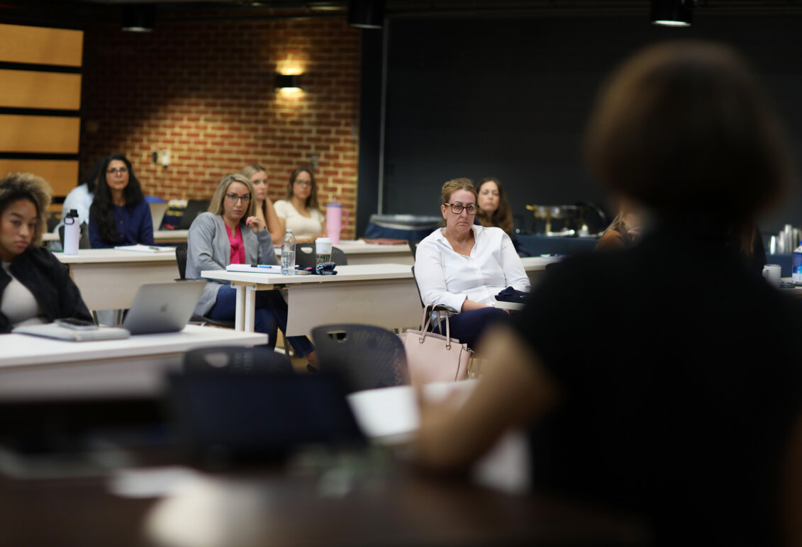 Students sit in a classroom with a brick wall in the background