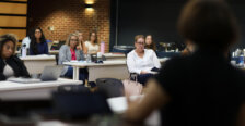 Students sit in a classroom with a brick wall in the background