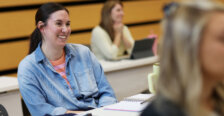 A woman wearing a denim shirt smiles as she sits in a classroom