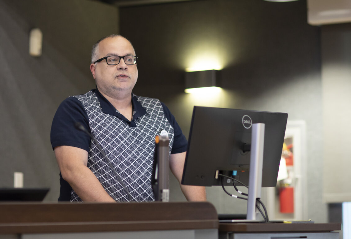 A man stands at a podium with a computer monitor in front of him