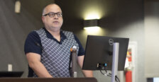 A man stands at a podium with a computer monitor in front of him