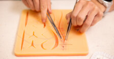 A close-up of a pair of hands practicing sutures on a flesh colored plastic mat. Photo by Parker Michels-Boyce.