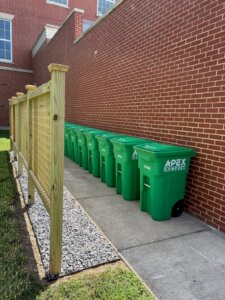 a line of composting bins against a brick wall outdoors on UMW's campus