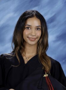 Student pictured in a black graduation gown in front of a blue backdrop