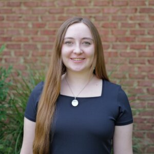 Student in a navy top pictured in front of foliage and a brick wall