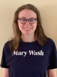 student with glasses in front of pale backdrop wears a navy Mary Wash t-shirt