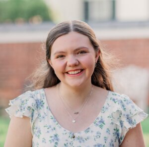 Student in a floral dress smiles in front of a blurry brick backdrop