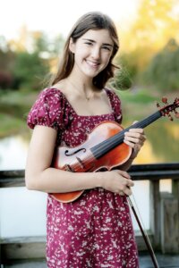 Student in red dress pictured holding a violin outdoors