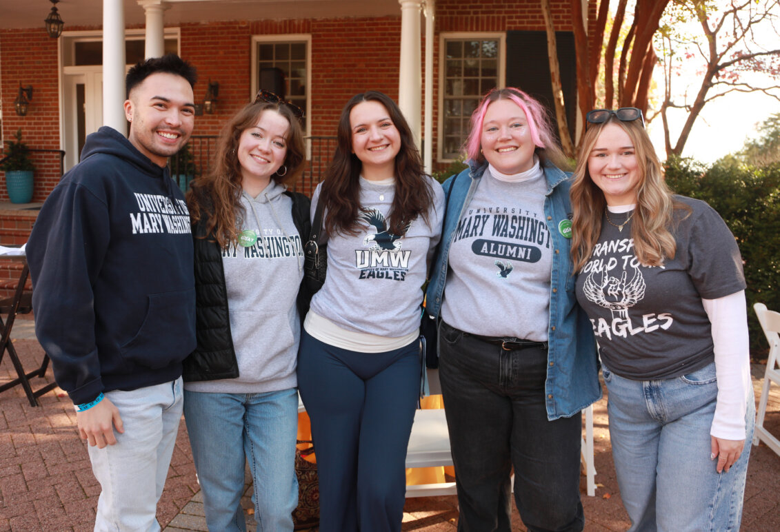 A group of five recent graduates wearing UMW shirts and hoodies in the Jepson Alumni Executive Center courtyard.
