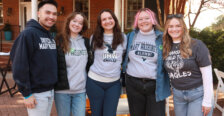 A group of five recent graduates wearing UMW shirts and hoodies in the Jepson Alumni Executive Center courtyard.