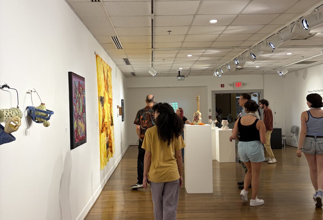 Visitors walk through a gallery featuring colorful wall-mounted artwork, sculptures and objects displayed on pedestals.