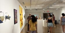 Visitors walk through a gallery featuring colorful wall-mounted artwork, sculptures and objects displayed on pedestals.