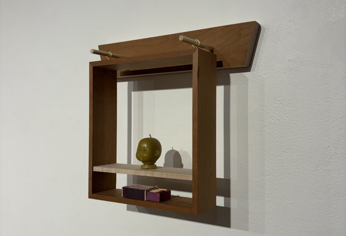 Small wooden wall-mounted shelf displaying a green sculpted head and two small rectangular objects.