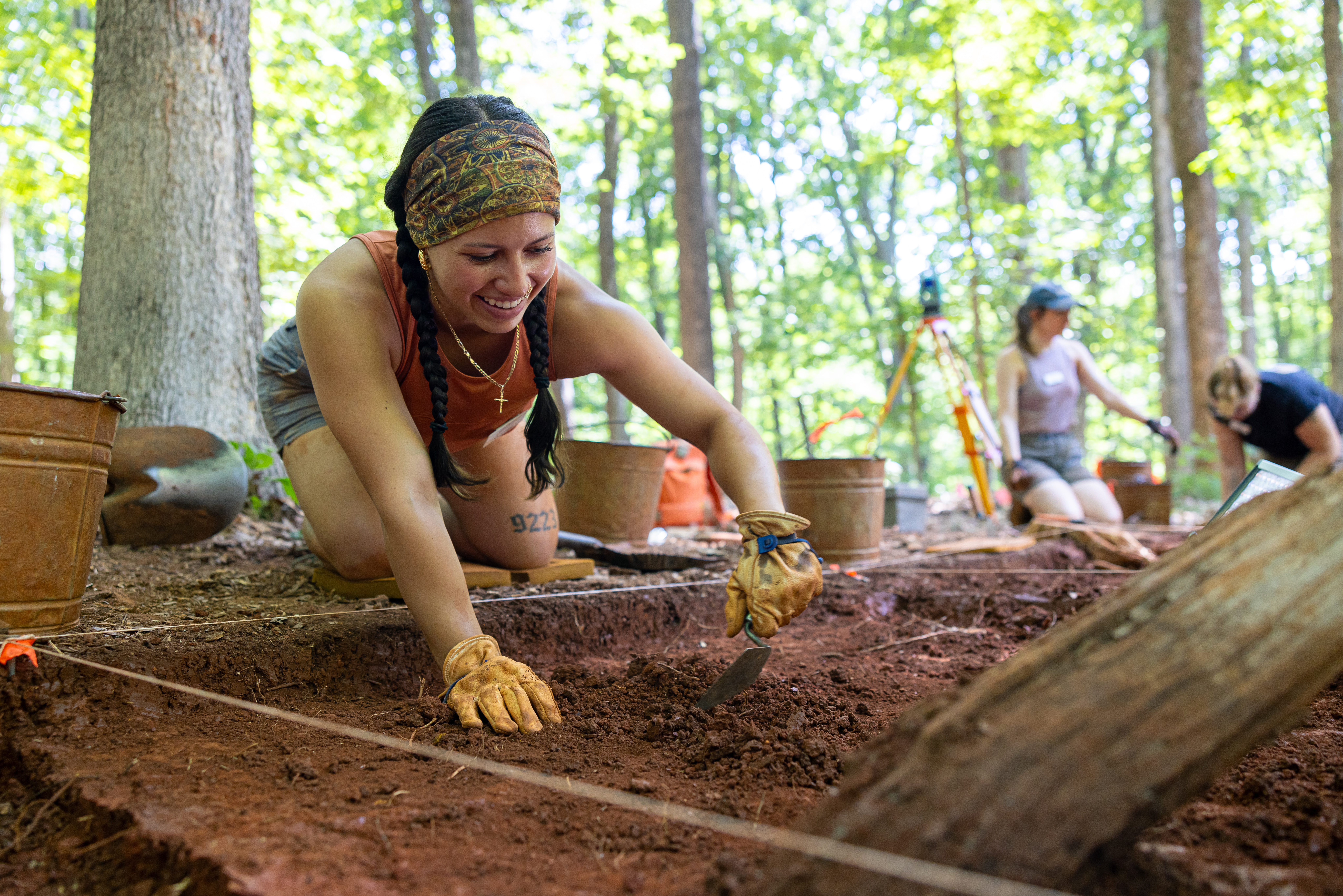 A girl wearing gloves digs in a squared-off section of dirt with a trowel