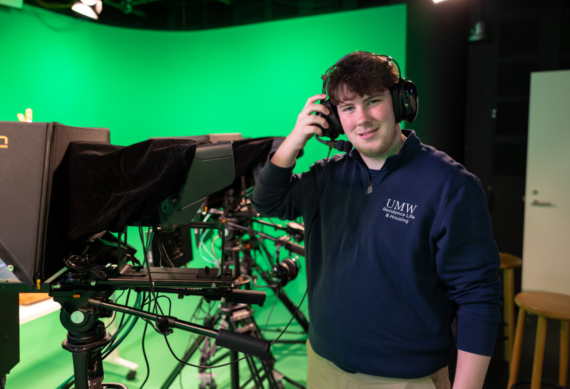 A male wearing headphones stands in a green room with cameras