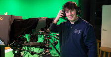 A male wearing headphones stands in a green room with cameras
