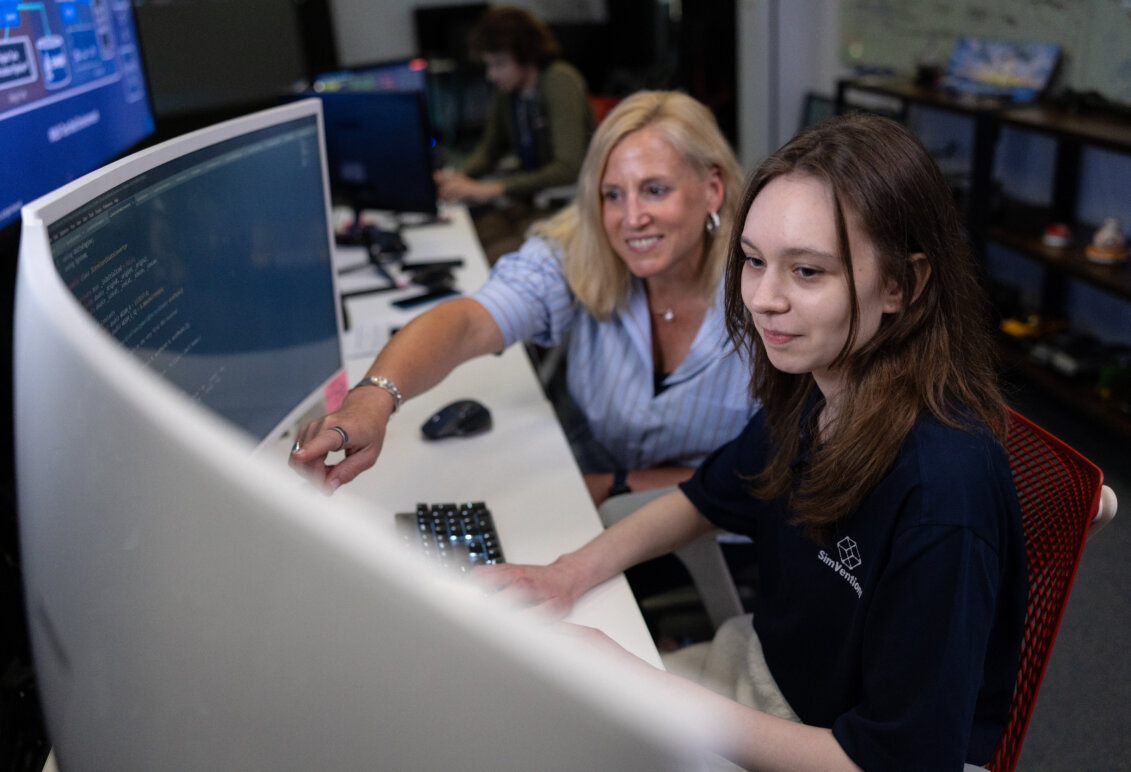A woman pointing at a computer monitor sits beside a female student