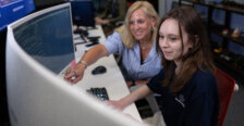A woman pointing at a computer monitor sits beside a female student