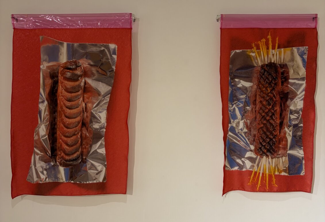 Two mixed-media artworks featuring sculpted, grilled food forms on reflective silver material and red fabric.